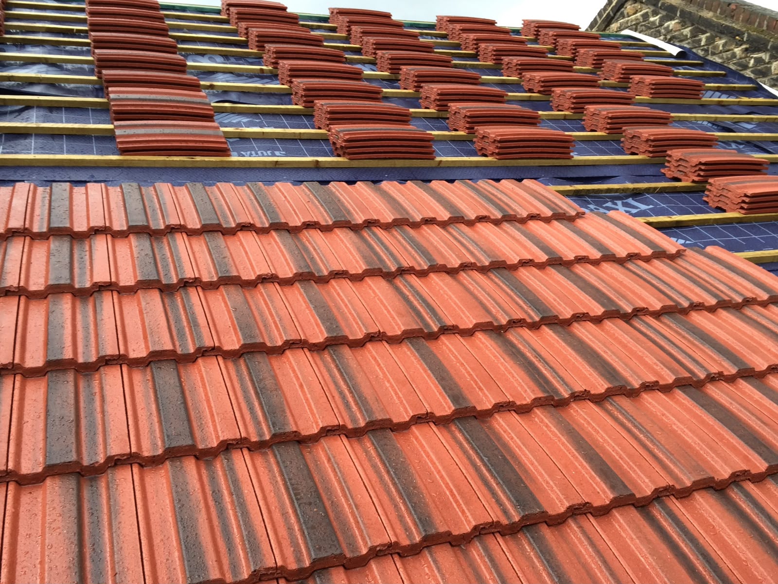 Terracotta roof tiles being installed over felt and battens